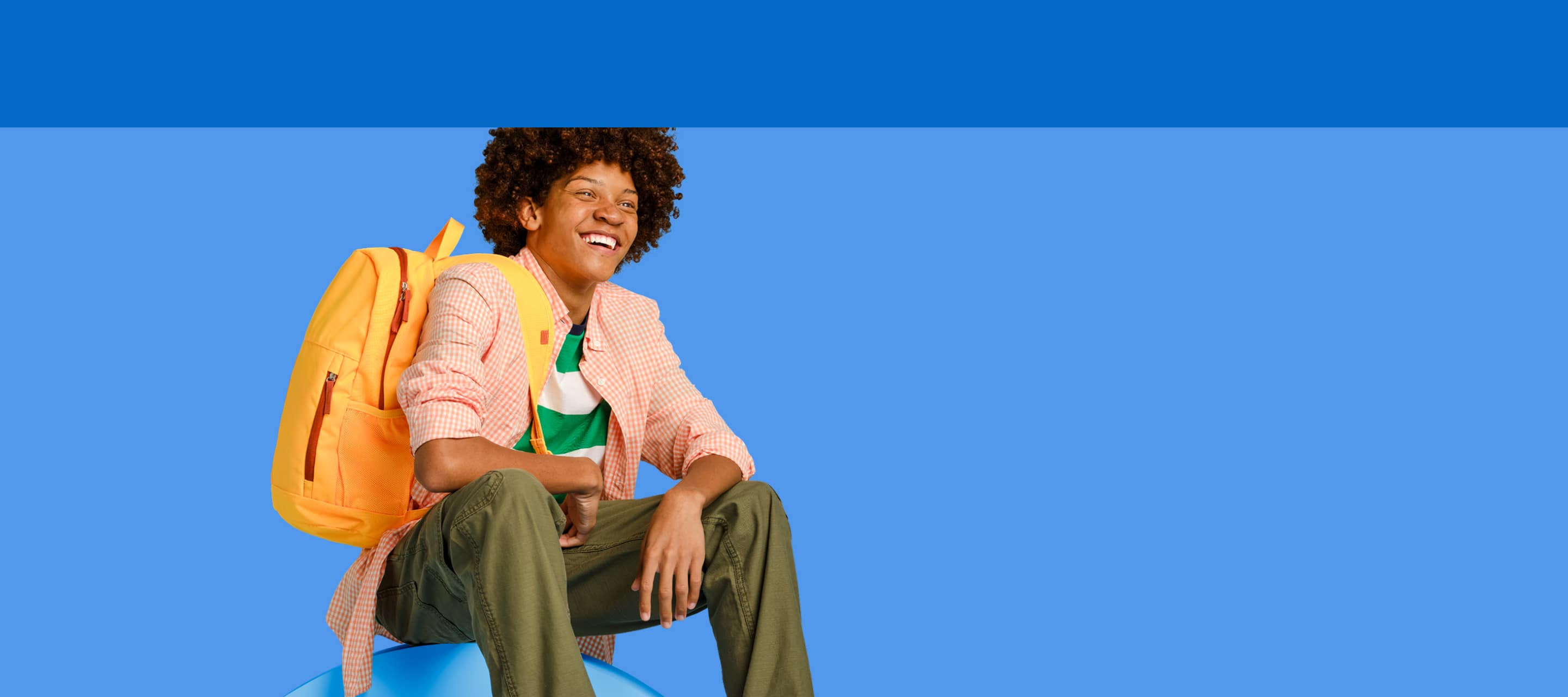 teenager in colorful clothing with a backpack on shoulder sitting against a cornflower blue background